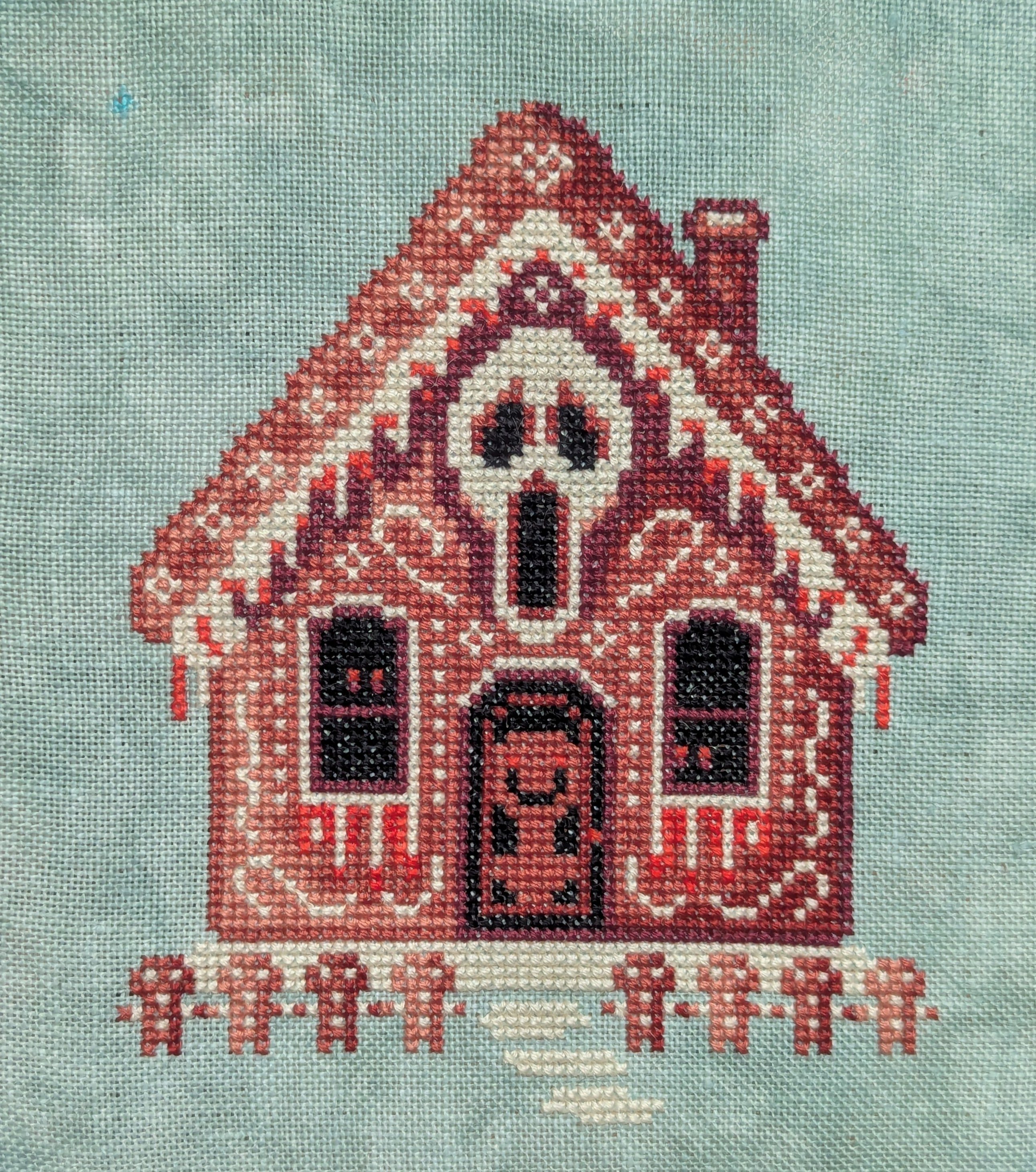Cross stitch of gingerbread house with a scream skull on it